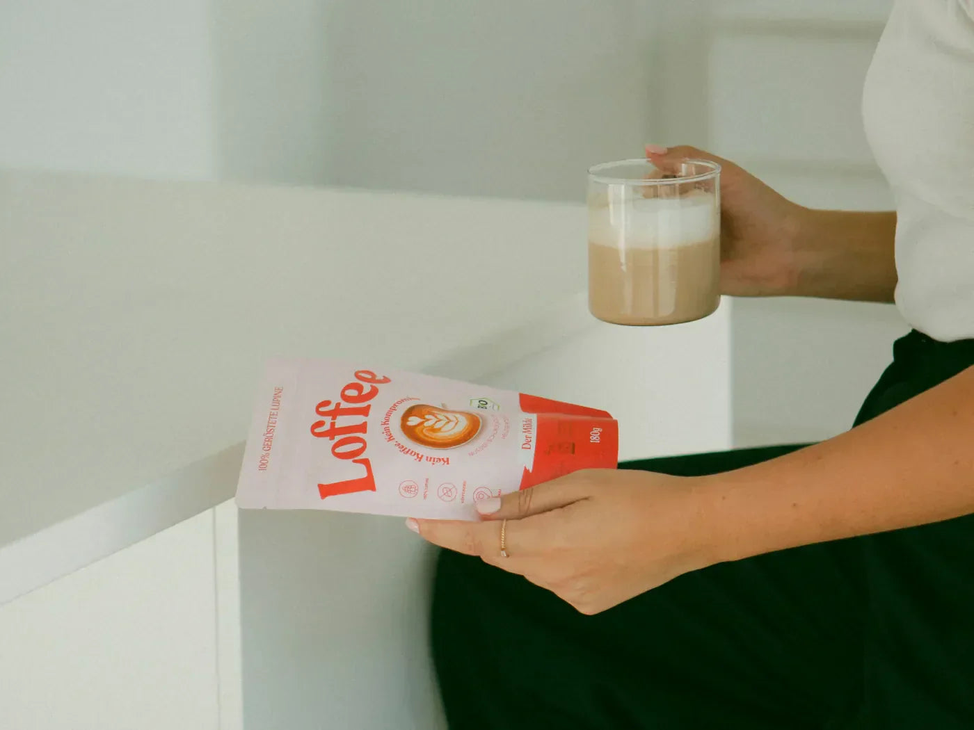 Lupinenkaffee zubereitet in einer Tasse in der linken Hand einer Frau. In der recht Hand hält sie eine Tüte Loffee.